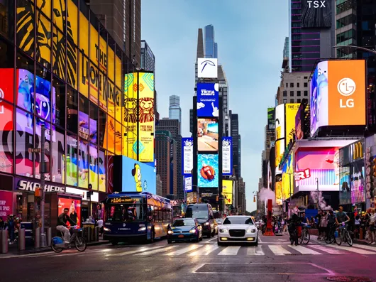 Digital billboards covering the buildings of a busy city square at dusk