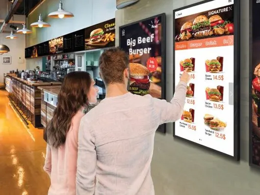 A couple choosing burgers from illuminated digital menu screens