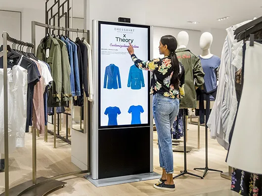 A shopper customising a jacket on a tall touchscreen kiosk between clothing rails